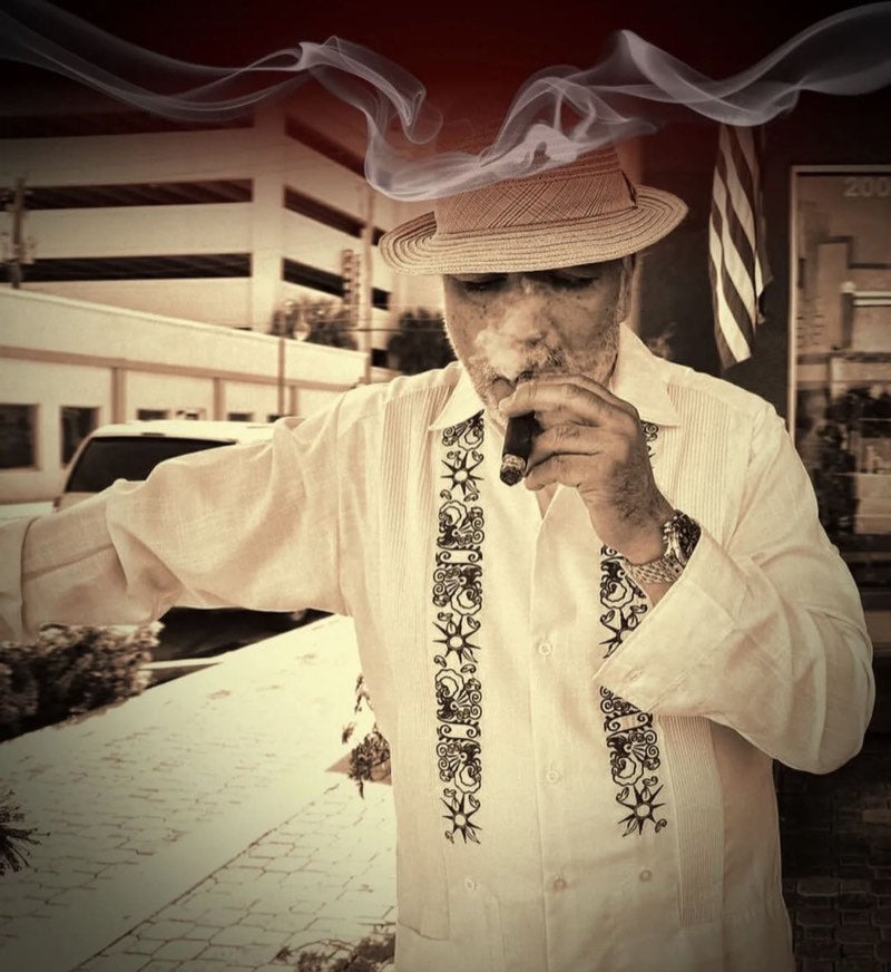 Felix Assouline in a straw hat and embroidered guayabera, smoking a cigar